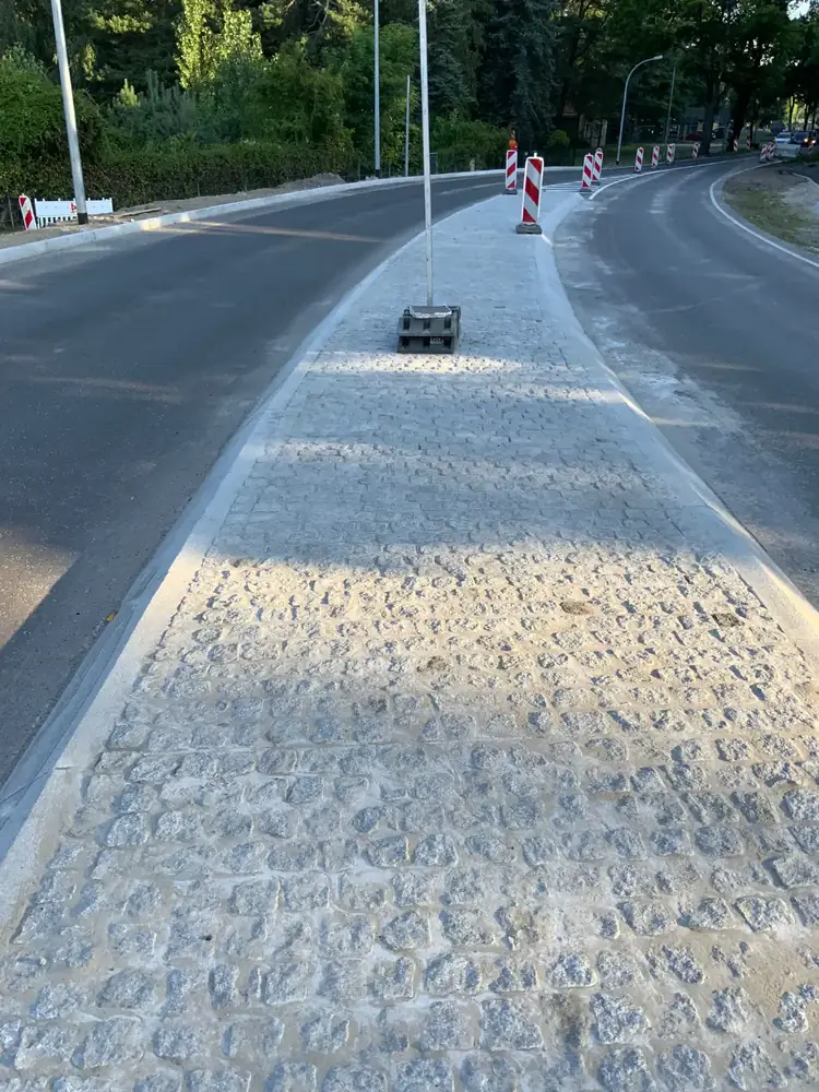 Neu verlegter Streifen aus Natursteinpflaster neben einer Asphaltstraße, Baustelle abgesperrt