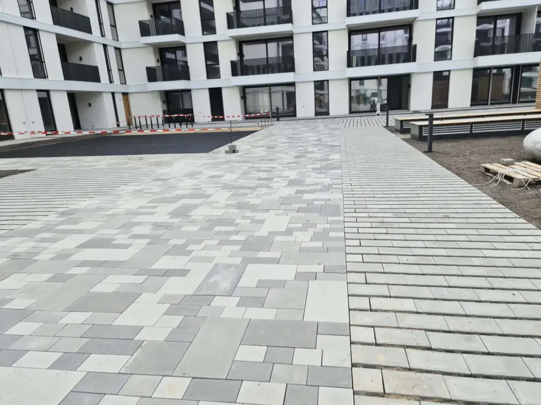 Fertig gepflasterte Hoffläche aus großformatigen grauen Betonplatten vor einem Wohnneubau