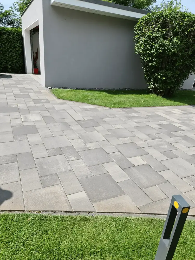 Hof aus grauen Betonsteinplatten in verschiedenen Formaten mit Rasenkante vor einem Gebäude